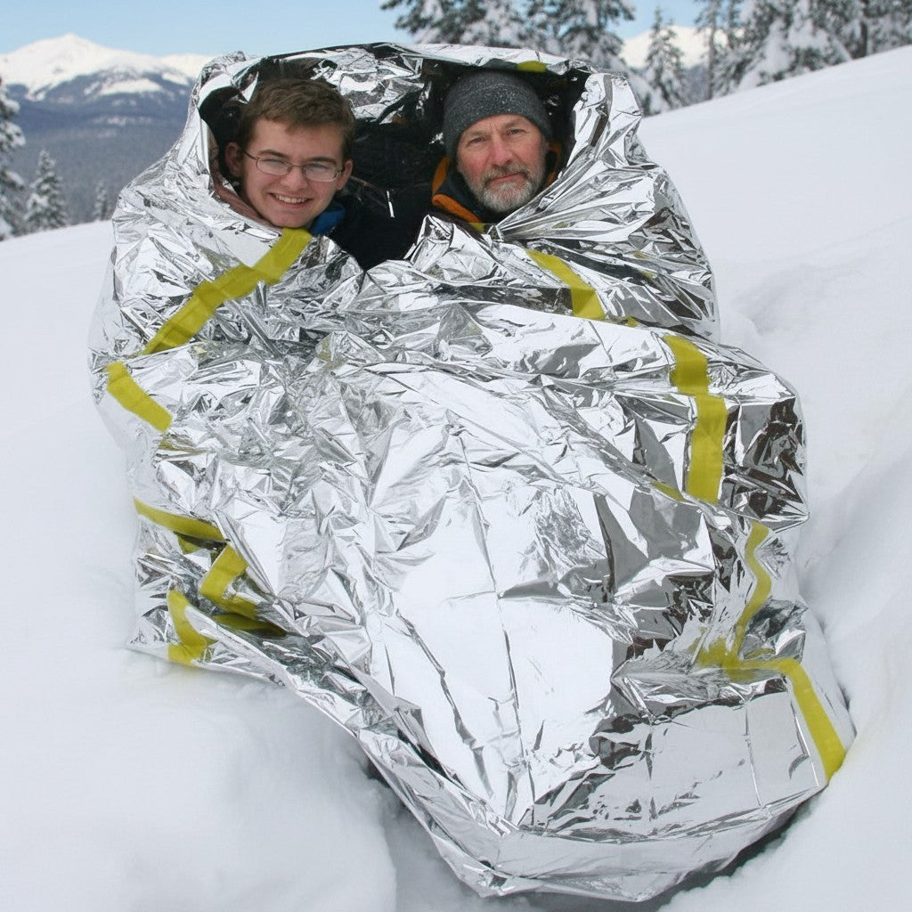Dos personas envueltas en un saco de dormir reflectante GERF SAFETY de Mylar plateado en un entorno nevado.